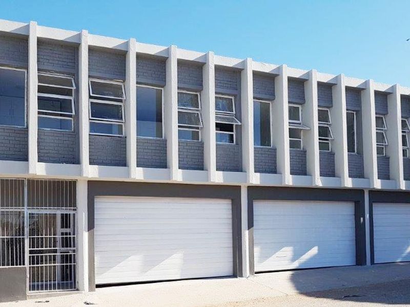 Front elevation of the apartment building featuring three ground-level garage doors and a row of upper-level windows with concrete architectural detailing.