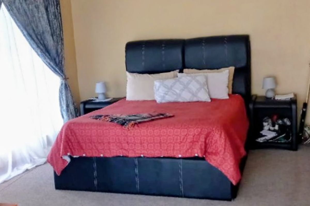 A standard bedroom featuring carpeted flooring and a large window with curtains.