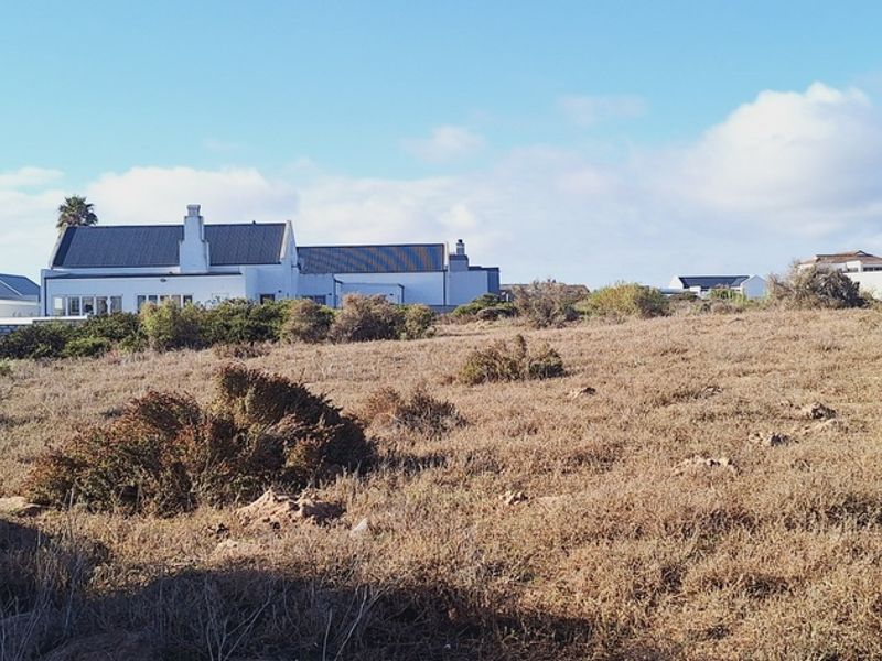 A view of a vacant residential plot featuring natural vegetation with established residential properties visible in the background.