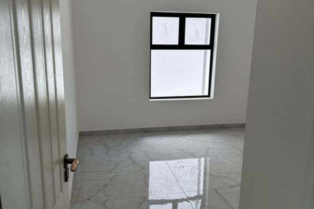 A bright, empty bedroom featuring polished marble-look floor tiles and a single window, providing a clean and neutral space ready for furnishing.