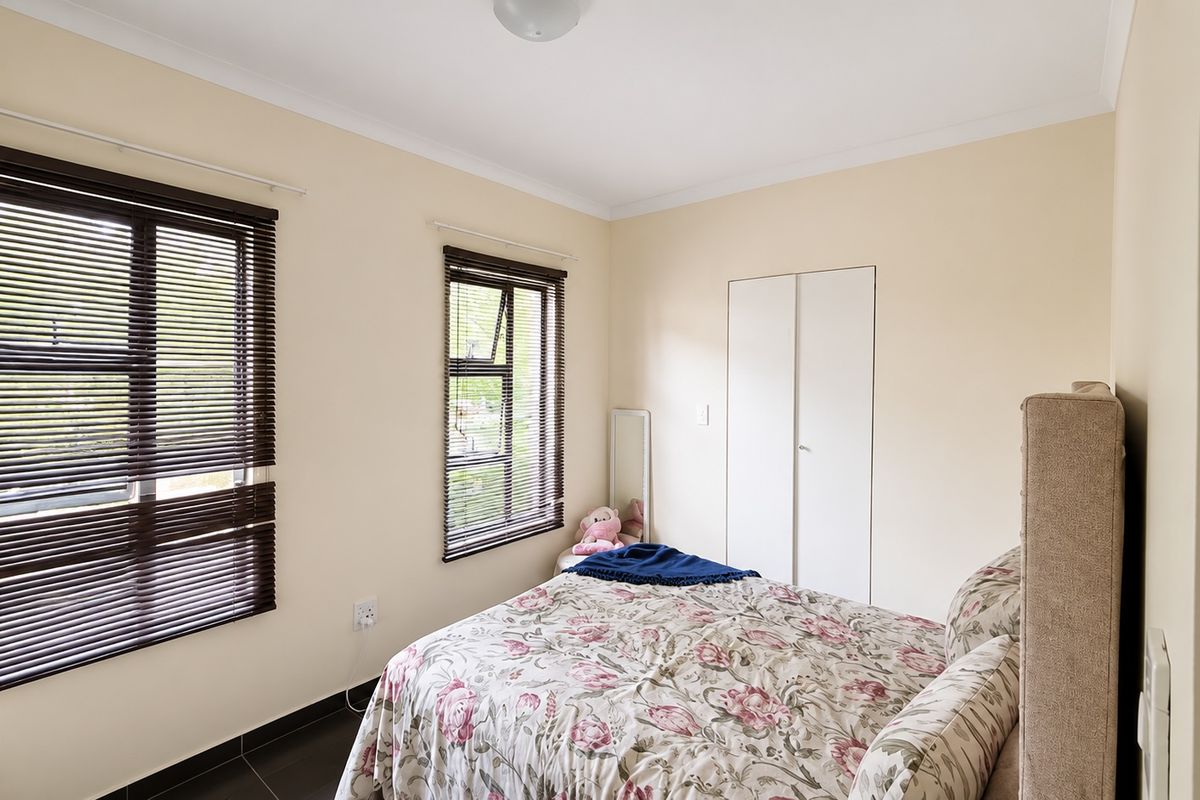 A bedroom featuring built-in cupboards, tiled flooring, and windows fitted with dark timber venetian blinds.