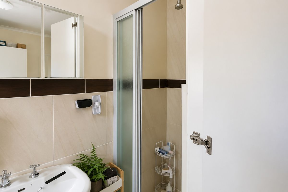 A functional bathroom featuring a built-in vanity with mirror cabinet, tiled walls with a decorative border, and a glass-enclosed shower stall.