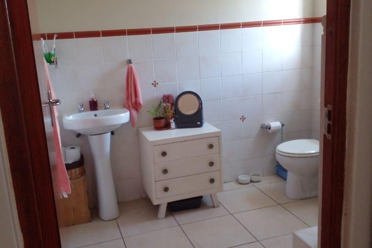 A functional bathroom featuring a pedestal basin, toilet, and neutral wall and floor tiling.