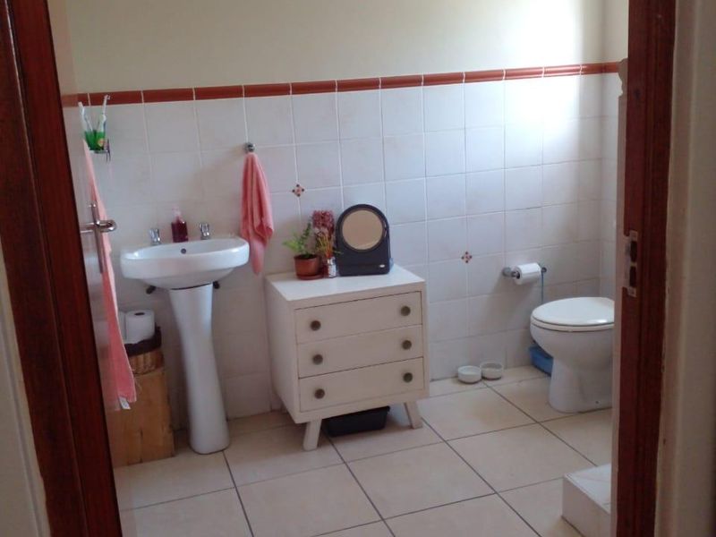 A functional bathroom featuring a pedestal basin, toilet, and neutral wall and floor tiling.