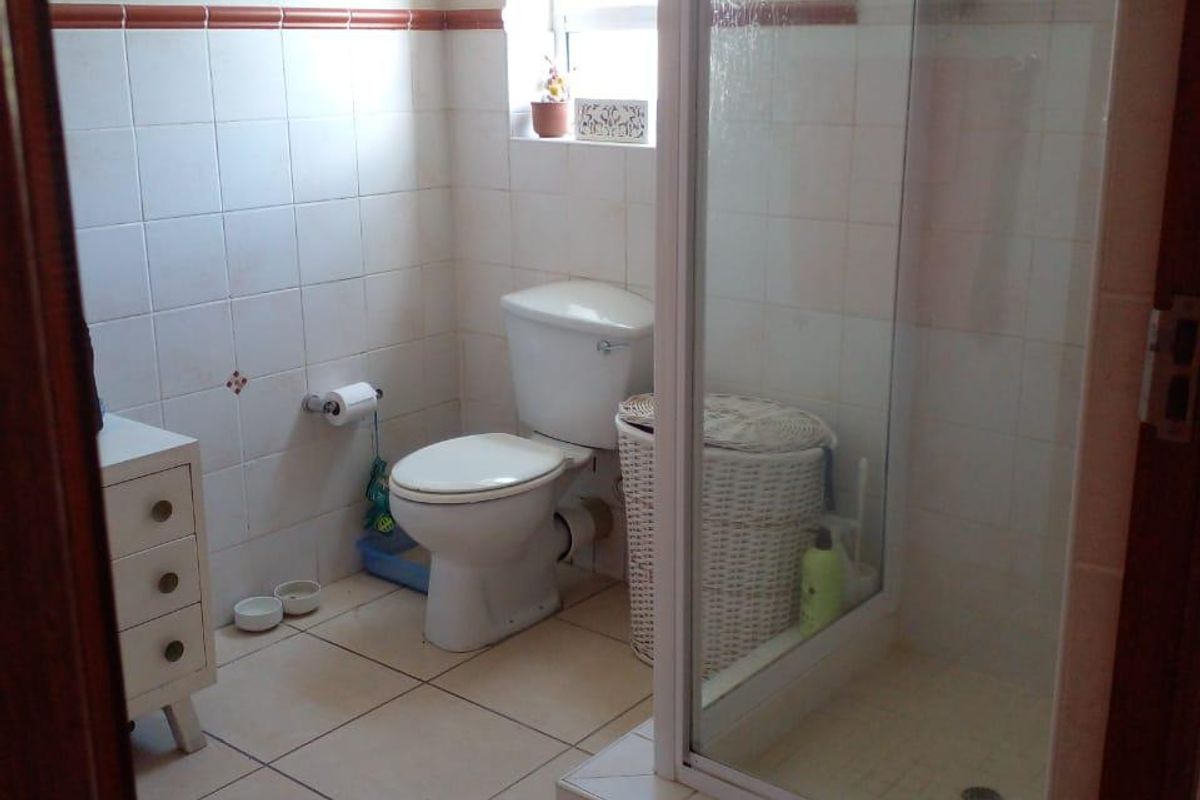 A functional bathroom featuring a shower enclosure, toilet, and neutral wall and floor tiling, offering a clean and practical layout.