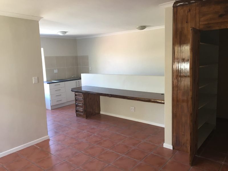 An open-plan living area featuring a functional kitchen corner with built-in cabinetry, a tiled backsplash, and a dedicated built-in wooden desk space.