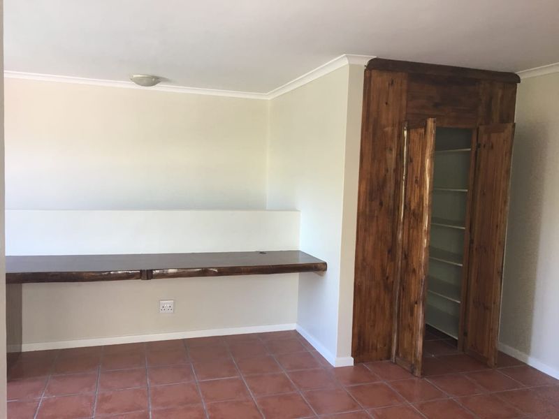A functional home office space featuring a built-in wooden desk, matching storage cupboard, and durable tiled flooring.