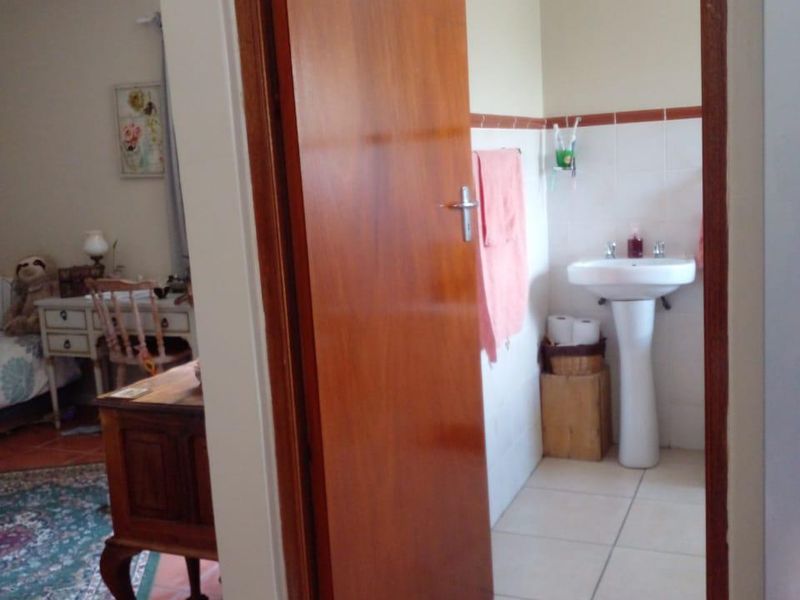 A functional bathroom featuring a pedestal basin and tiled finishes, accessible via a timber door from the adjacent living area.