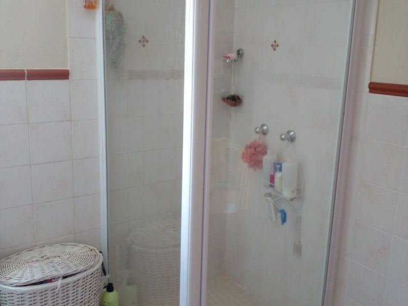 A functional bathroom featuring a corner shower enclosure with white frame and tiled wall finishes.