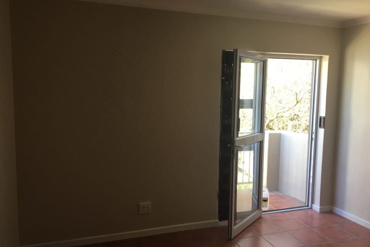 An empty living area featuring terracotta floor tiles and a glass door providing direct access to an outdoor balcony space.