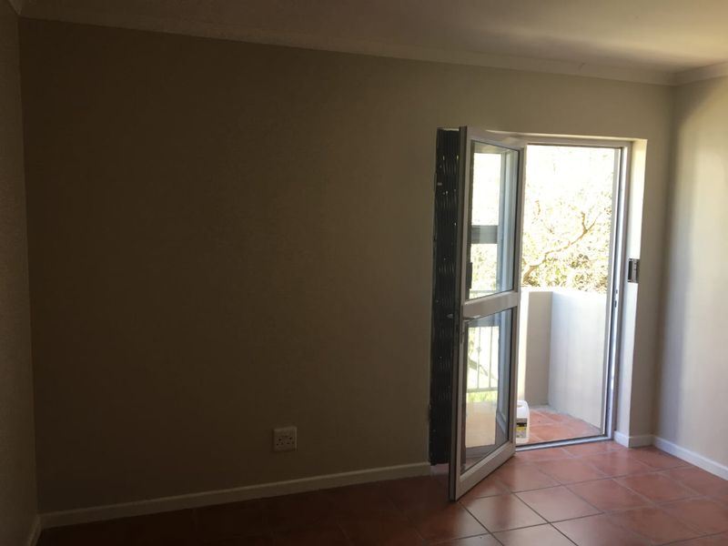 An empty living area featuring terracotta floor tiles and a glass door providing direct access to an outdoor balcony space.