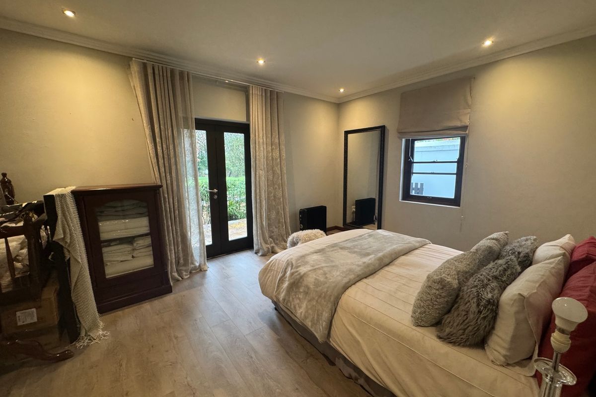 A well-lit bedroom featuring wood-look flooring, recessed ceiling lighting, and direct access to the outdoors through a glass-paneled door.