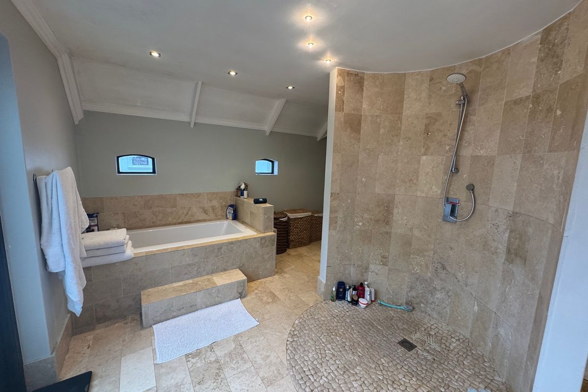 Spacious bathroom featuring a built-in bathtub with stone surround, a curved walk-in shower with pebble flooring, and recessed ceiling lighting.