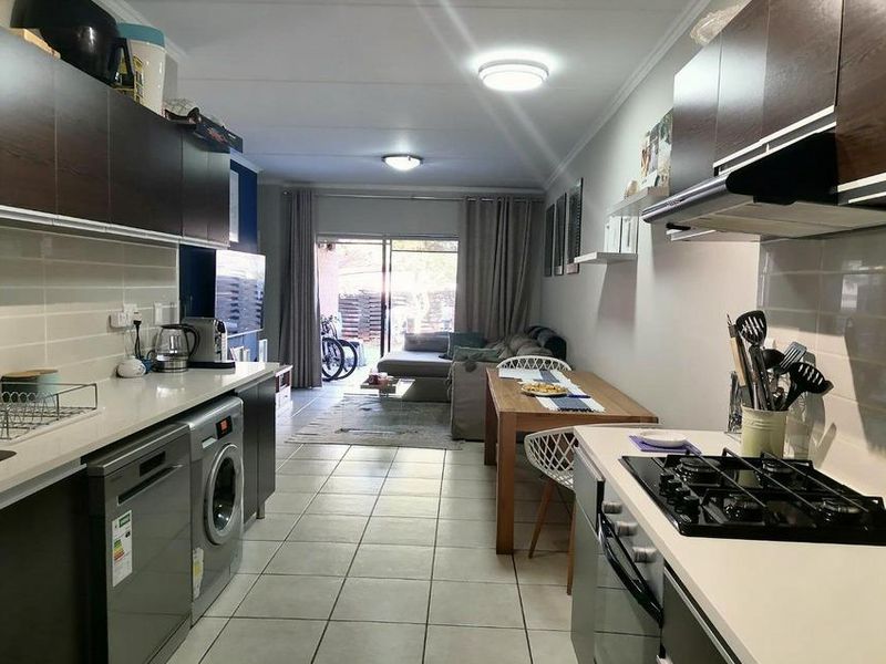 Open-plan living area featuring a modern kitchen with built-in cabinetry, gas hob, and tiled flooring, leading directly to an outdoor patio area.