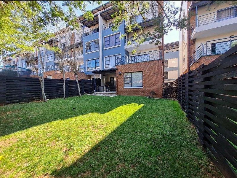 Rear view of a modern apartment complex featuring a private garden, timber fencing, and elevated balconies with brick and blue facade finishes.