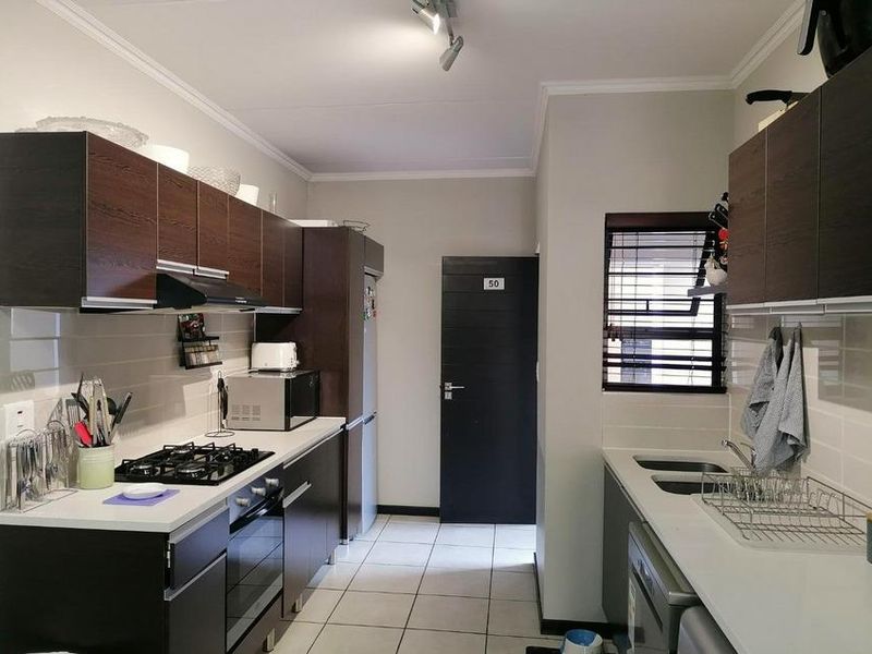 A functional kitchen featuring dark wood-look cabinetry, a gas hob with extractor, built-in oven, and a double sink with tiled flooring.