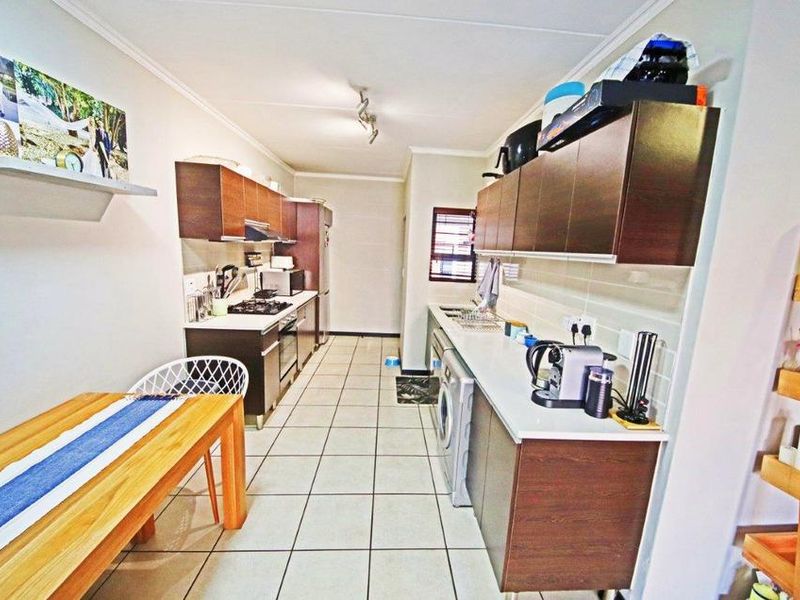 A functional galley-style kitchen featuring dark wood cabinetry, light countertops, tiled flooring, and integrated laundry facilities.