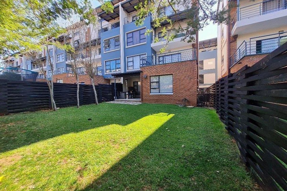 Rear view of a modern apartment complex featuring a private garden, timber fencing, and elevated balconies with brick and blue facade finishes.