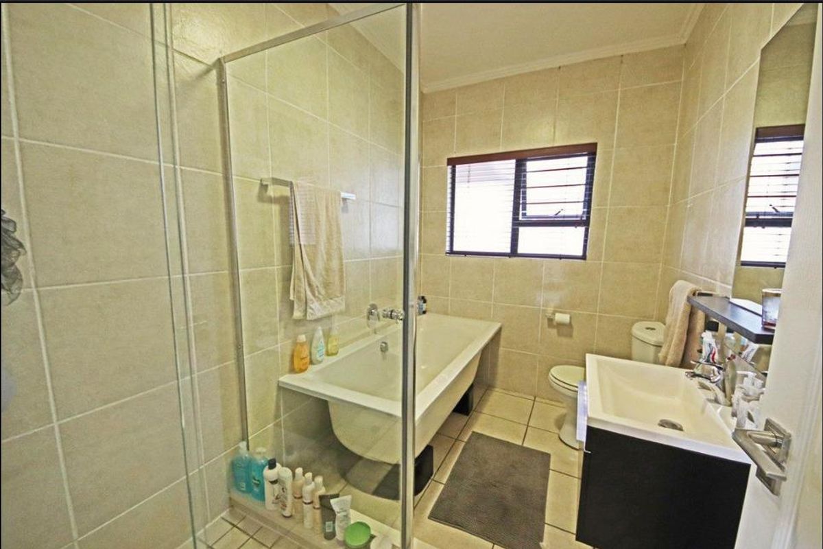 A functional bathroom featuring a bathtub, separate glass-enclosed shower, vanity basin, and toilet with neutral wall and floor tiling.