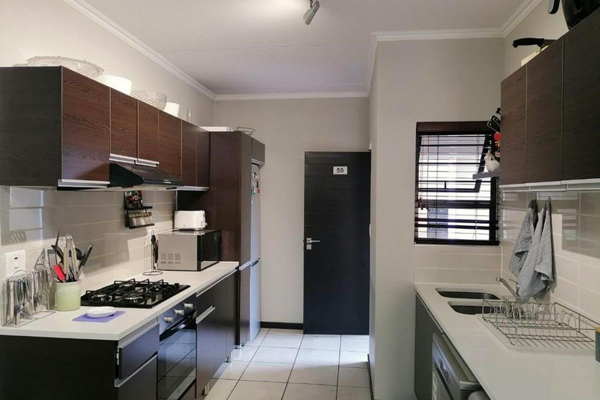 A functional kitchen featuring dark wood-look cabinetry, a gas hob with extractor, built-in oven, and a double sink with tiled flooring.
