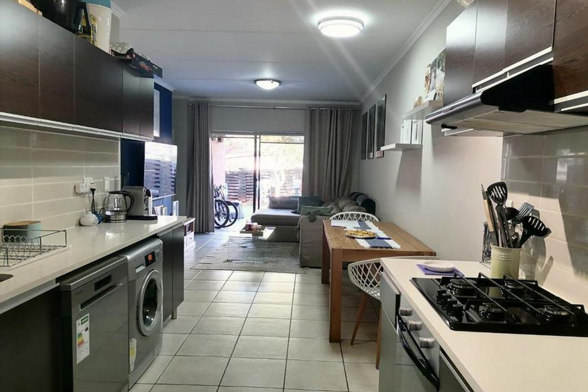 Open-plan living area featuring a modern kitchen with built-in cabinetry, gas hob, and tiled flooring, leading directly to an outdoor patio area.