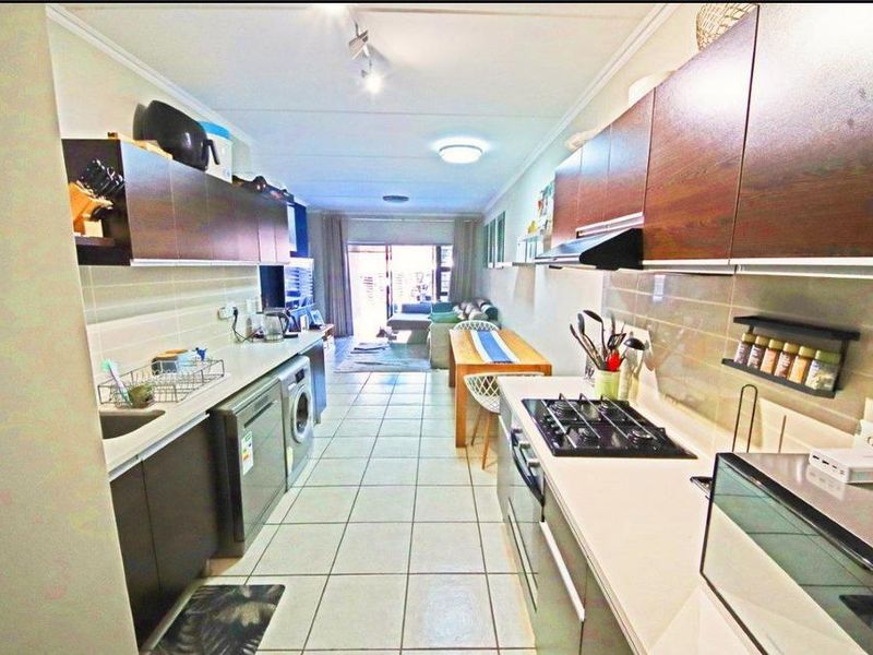 Open-plan kitchen and living area featuring dark wood cabinetry, gas hob, tiled flooring, and direct access to the patio area.