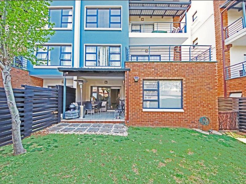 Rear view of the apartment building featuring a private garden, a covered tiled patio, and upper-level balconies with metal railings.