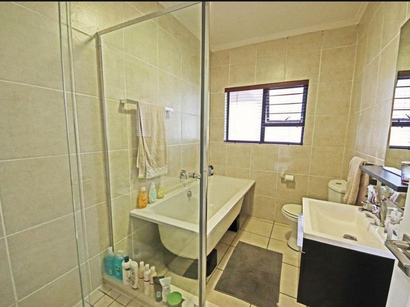 A functional bathroom featuring a bathtub, separate glass-enclosed shower, vanity basin, and toilet with neutral wall and floor tiling.