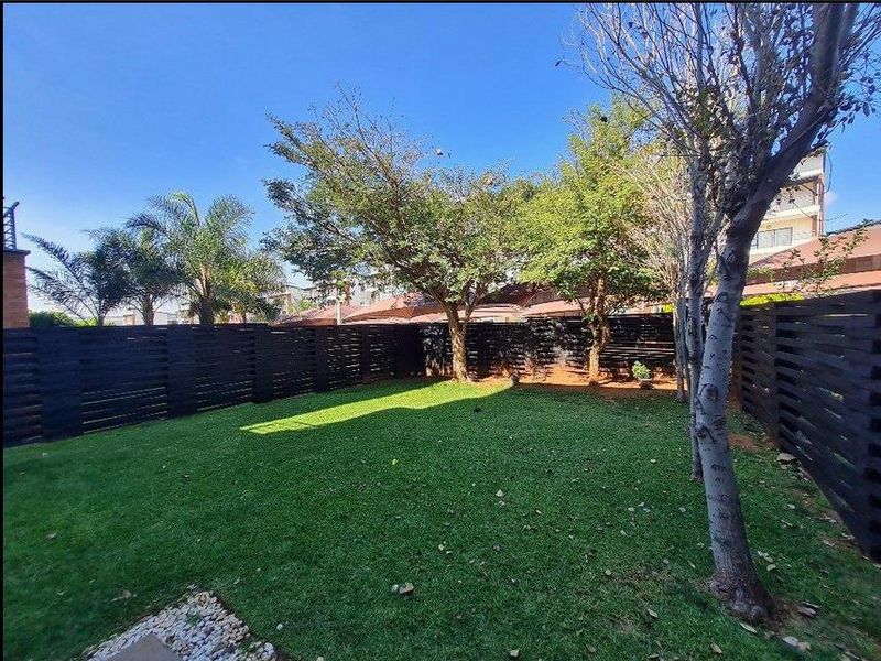 A private rear garden featuring a well-maintained lawn, mature trees, and modern timber slat perimeter fencing.