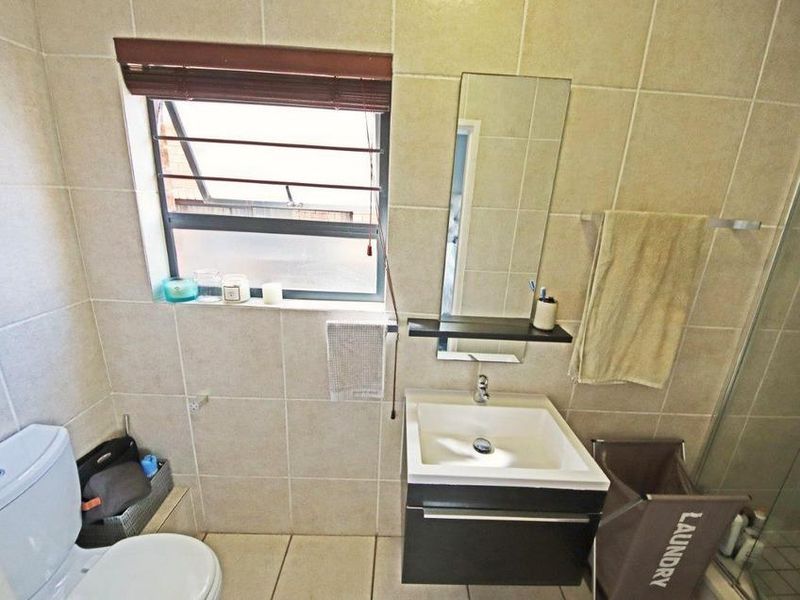 A functional bathroom featuring a modern vanity cabinet, ceramic basin, wall-mounted mirror, toilet, and a glass-enclosed shower with neutral wall and floor tiling.