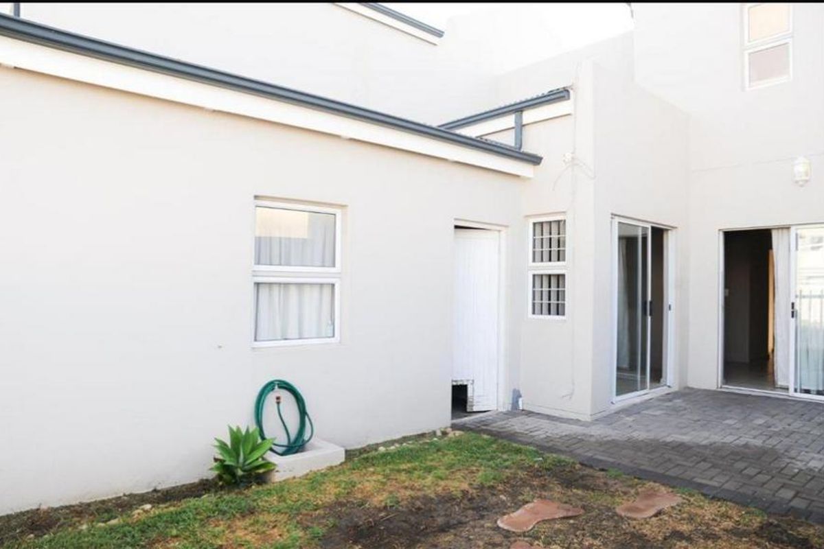 Rear view of the townhouse featuring a paved patio area, sliding glass doors, and a small garden space.