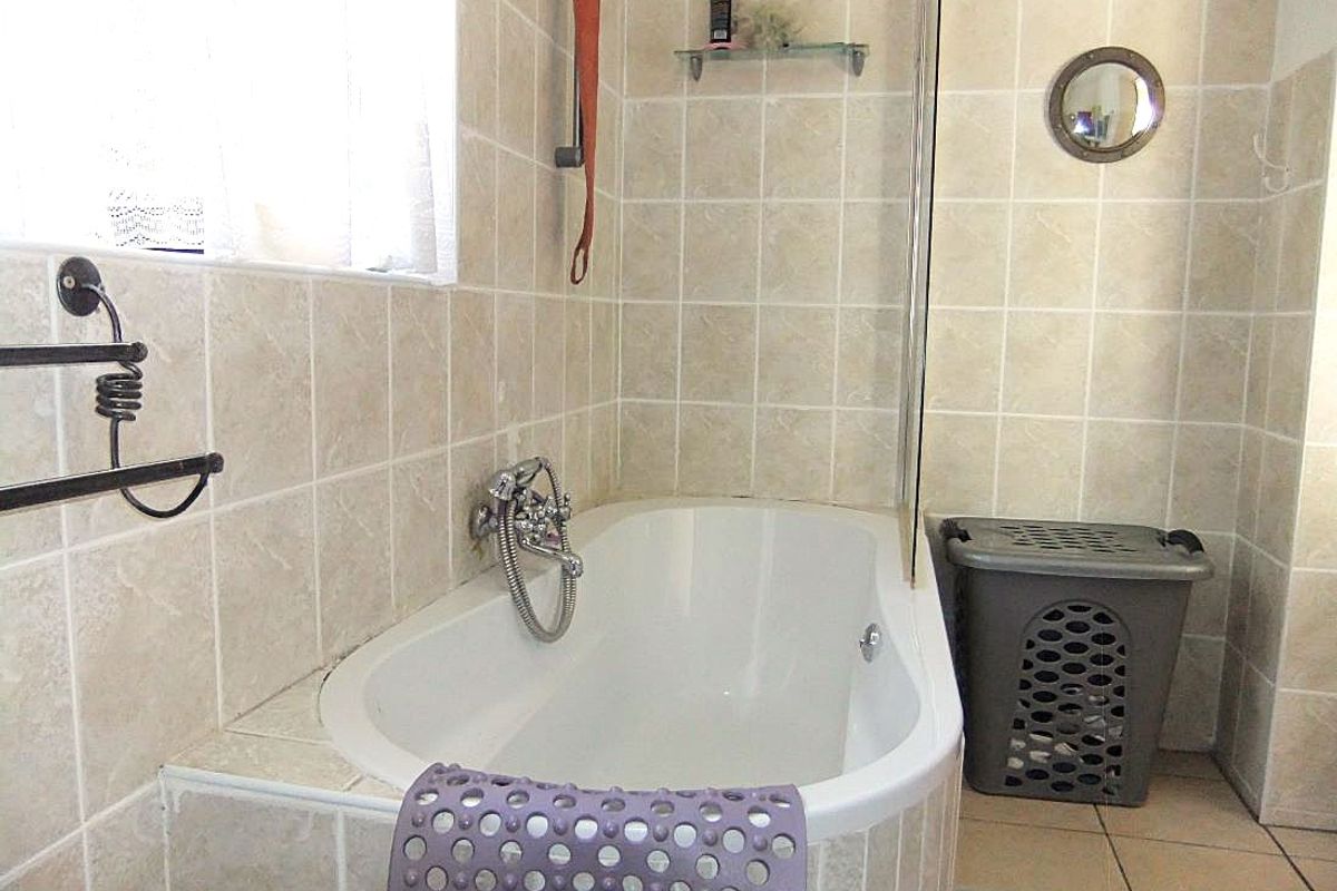 A functional bathroom featuring a built-in bathtub with a shower mixer, glass screen, and neutral ceramic tiling throughout.