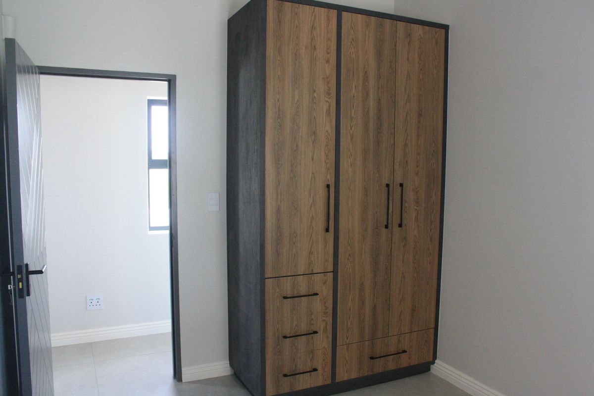 A clean, modern bedroom featuring a contemporary wood-finish built-in wardrobe with black hardware and neutral tiled flooring.