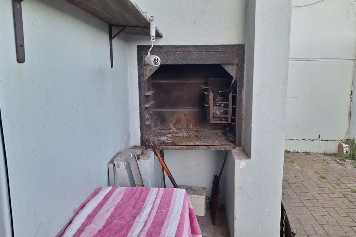 Outdoor built-in braai area featuring a masonry structure and paved courtyard space, requiring maintenance and cosmetic updates.