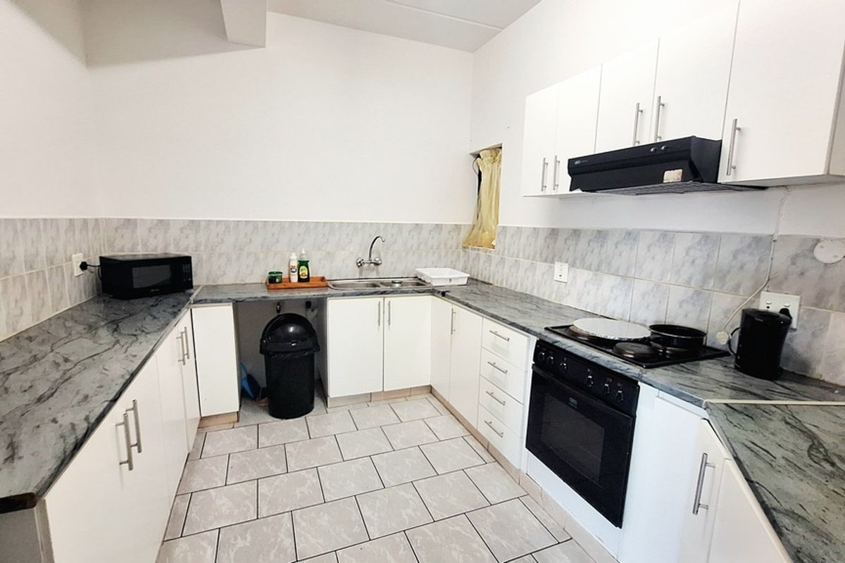 A functional kitchen featuring white cabinetry, dark marble-effect countertops, tiled splashbacks, and a built-in oven with an extractor fan.
