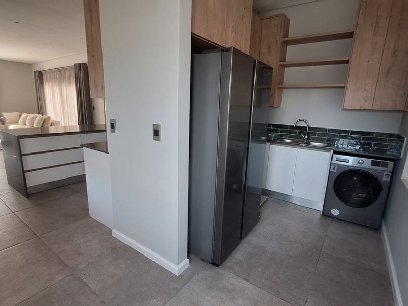 A modern, well-appointed scullery featuring sleek cabinetry, tiled backsplash, and integrated laundry facilities, conveniently positioned adjacent to the main living area.