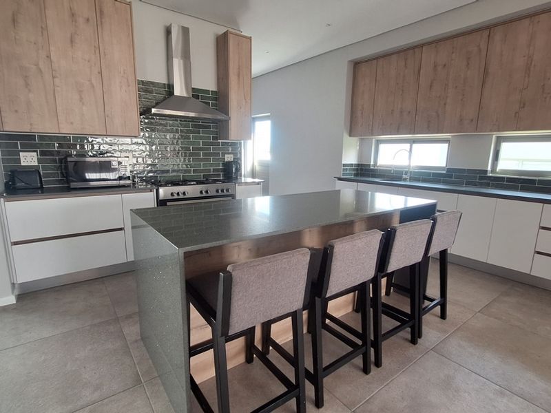 Modern kitchen featuring a large central island with stone countertops, sleek wood-tone and white cabinetry, stainless steel appliances, and a stylish tiled backsplash.