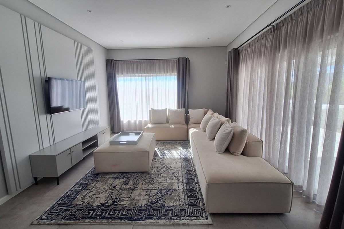 A modern, well-lit living room featuring a custom media wall, large format floor tiles, and expansive windows with floor-to-ceiling curtains.