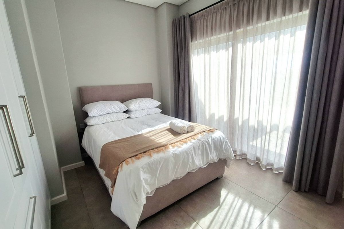 A well-maintained bedroom featuring neutral tiled flooring, built-in cupboards, and a large sliding glass door providing ample natural light.