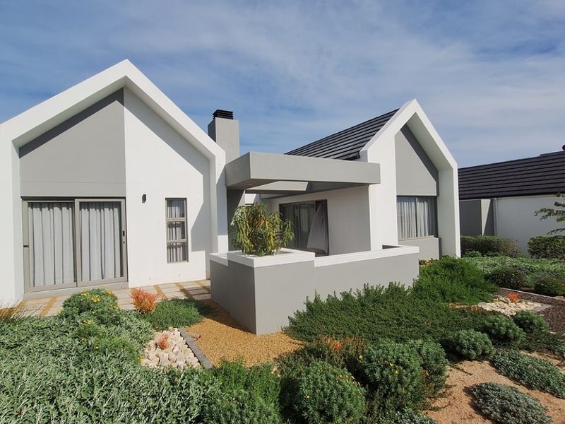 Modern rear elevation of a house featuring a contemporary gabled roof design, covered patio area, and well-maintained landscaped garden.