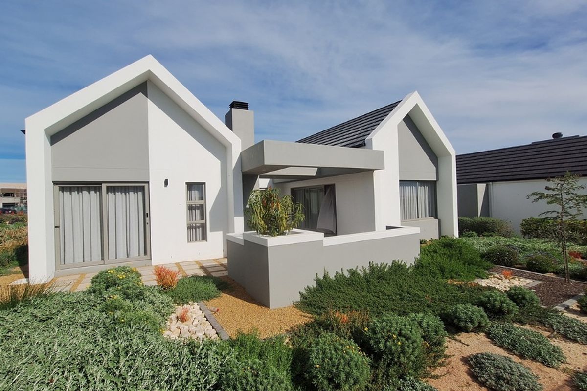 Modern rear elevation of a house featuring a contemporary gabled roof design, covered patio area, and well-maintained landscaped garden.
