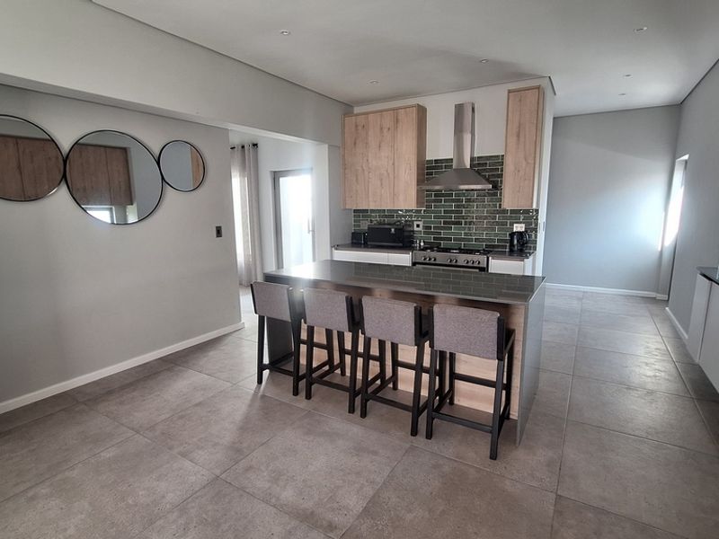Modern open-plan kitchen featuring a central island, wood-finish cabinetry, subway tile backsplash, and sleek tiled flooring in a contemporary living space.