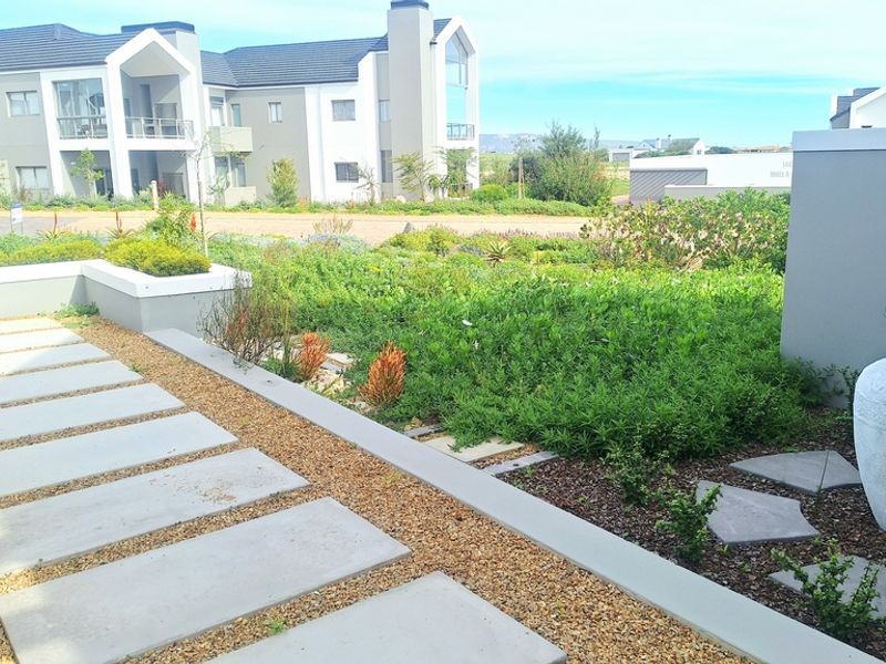 A well-maintained landscaped garden featuring concrete paver pathways, gravel beds, and a modern retaining wall in a residential estate setting.