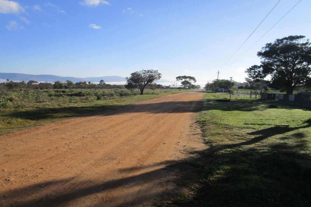 A view of an unpaved residential street with utility infrastructure and surrounding natural landscape.