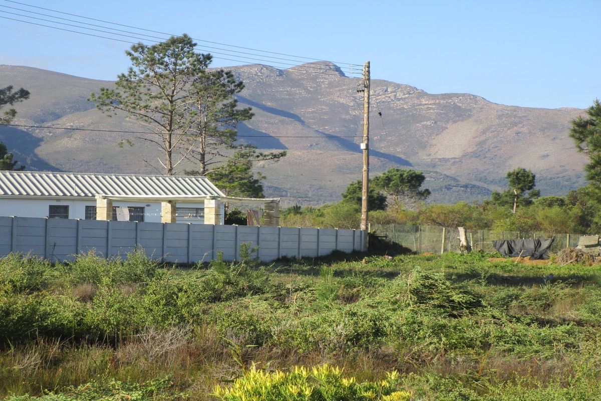 View of a residential property with a precast concrete boundary wall and corrugated metal roof, set against a scenic mountain backdrop.