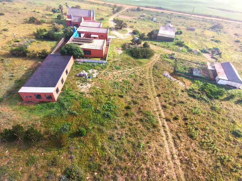 Aerial view of a small holding property featuring multiple outbuildings, solar panel installations, and expansive surrounding land.