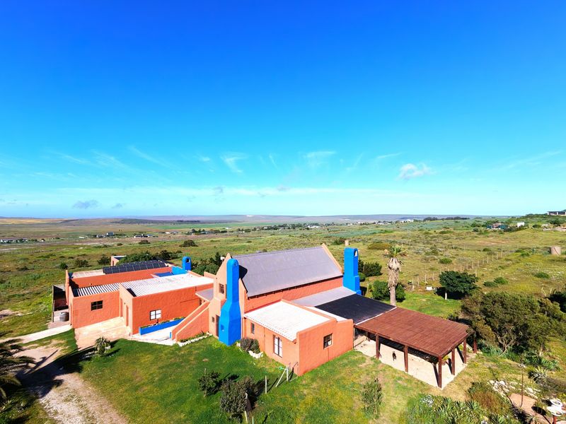 Aerial view of a large rural small holding featuring a terracotta-colored building with blue chimneys, solar panels, and a covered patio area.