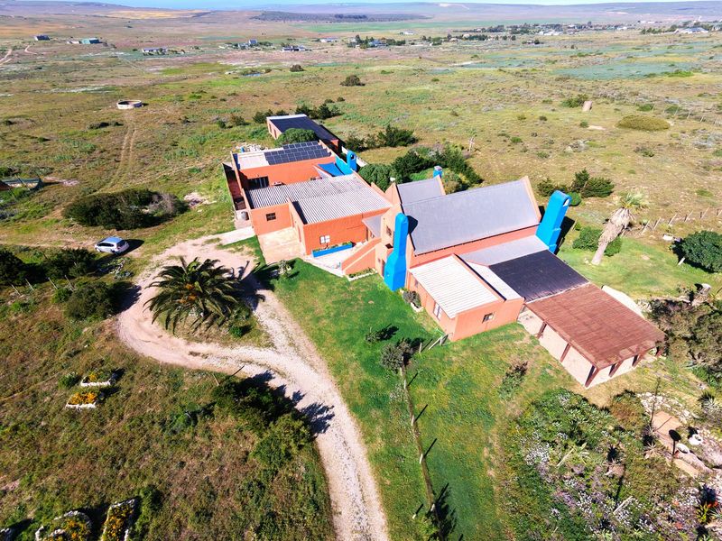 Aerial view of a rural small holding property featuring multiple interconnected buildings with corrugated roofing, solar panels, and surrounding natural landscape.