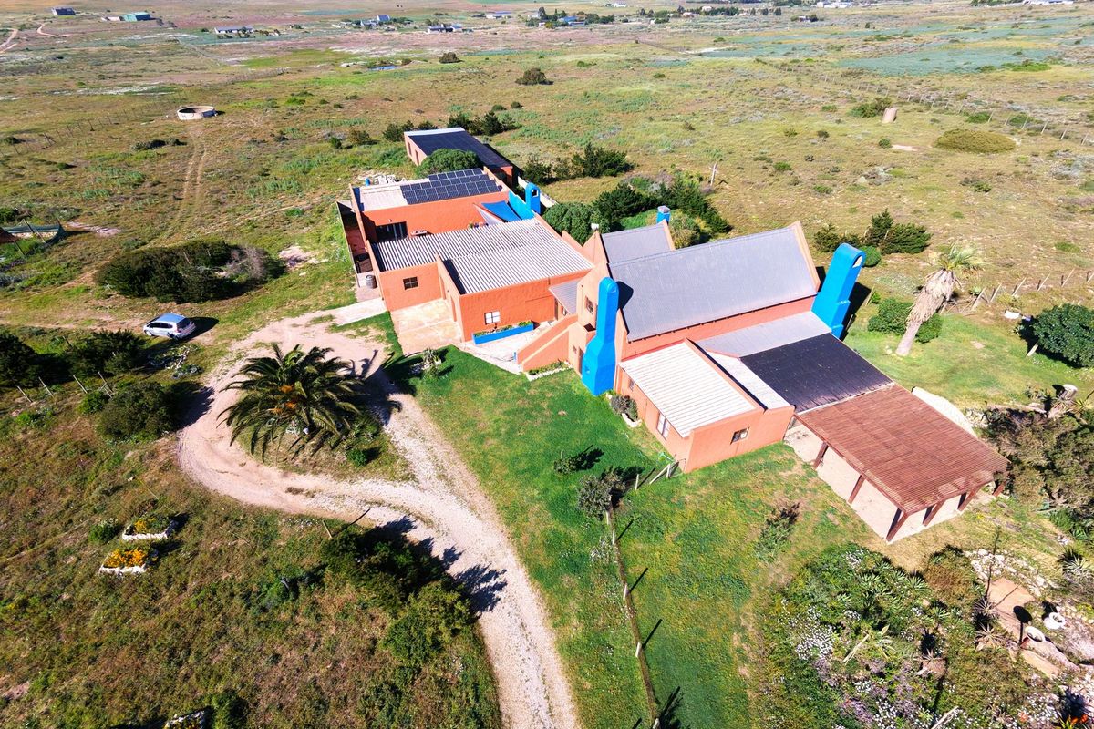 Aerial view of a rural small holding property featuring multiple interconnected buildings with corrugated roofing, solar panels, and surrounding natural landscape.