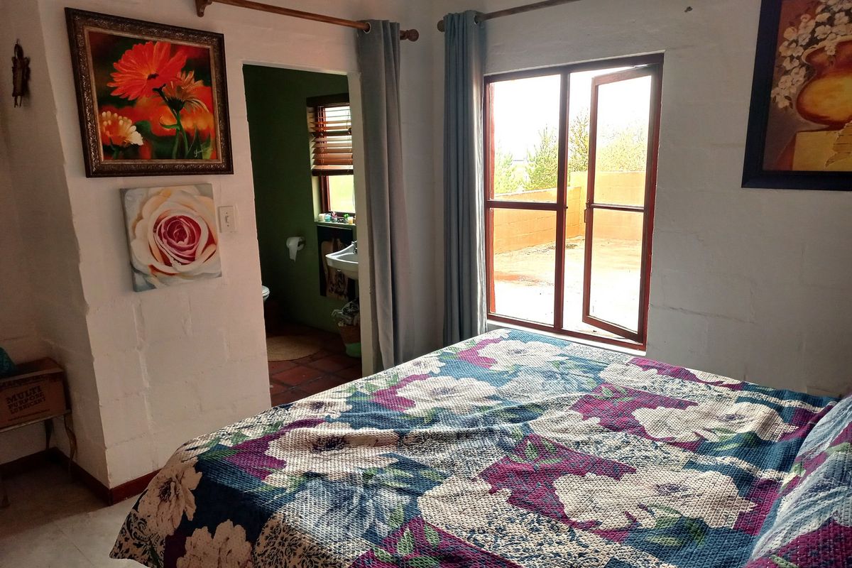 A bedroom featuring tiled flooring, a casement window with garden views, and an adjoining en-suite bathroom.